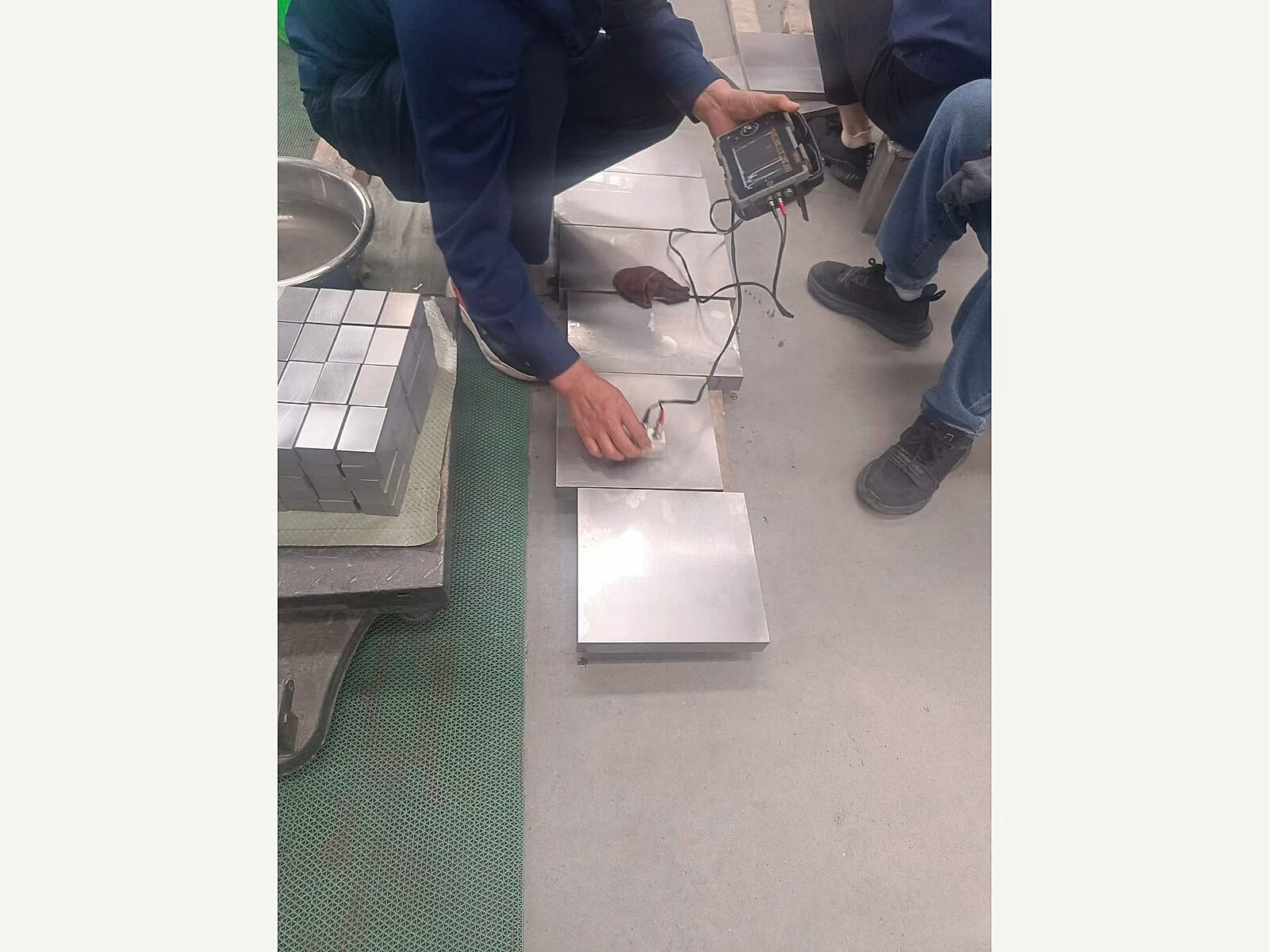 Inspection of titanium plate samples with a handheld device, showing the verification layer buyers need before accepting a new composition route.