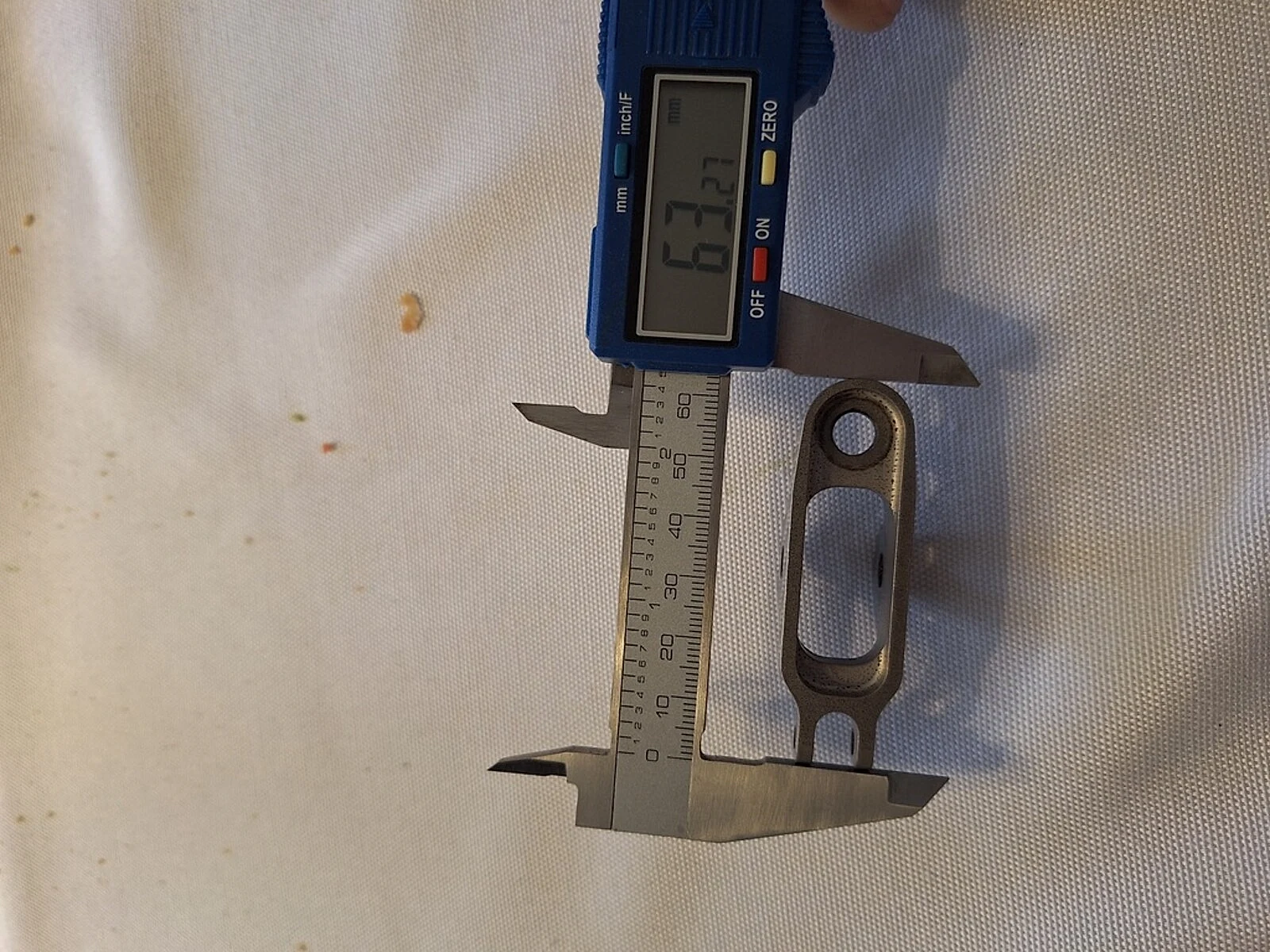 A caliper measurement on a small machined titanium-like part, showing why stockpile and traceability claims still need dimensional and lot-release checks.